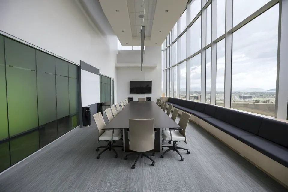 A long boardroom table with chairs beside floor-to-ceiling windows.